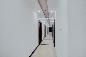 Un pasillo largo y estrecho con paredes blancas y piso de baldosas, que conduce a una puerta al final.