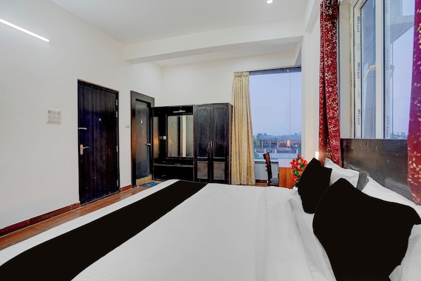 Habitación de hotel con una cama grande, un armario, un espejo, una ventana con cortinas y vistas a la ciudad.