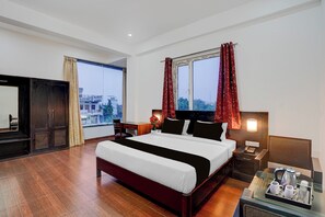 Habitación de hotel con una cama grande, mesitas de noche, un escritorio y vistas a la ciudad por la ventana.