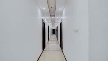 Un largo pasillo estrecho con paredes blancas y piso de baldosas, que conduce a varias puertas.
