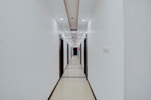 Un largo pasillo estrecho con paredes blancas y piso de baldosas, que conduce a varias puertas.