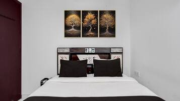A bedroom with a bed, a headboard with a decorative panel, and three wall-mounted paintings of trees.