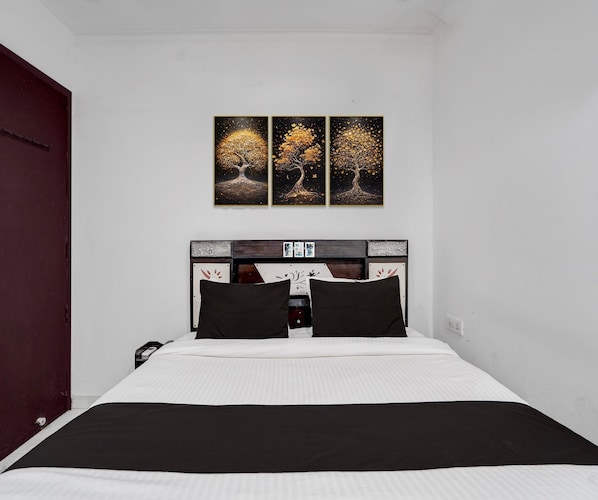 A bedroom with a bed, a headboard with a decorative panel, and three wall-mounted paintings of trees. - Deluxe Townhouse Huda Market (Gurugram)