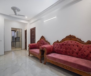 A spacious room with a large, ornate red sofa set against a white wall, a ceiling fan, and a door leading to another room. - Deluxe Townhouse Huda Market (Gurugram)