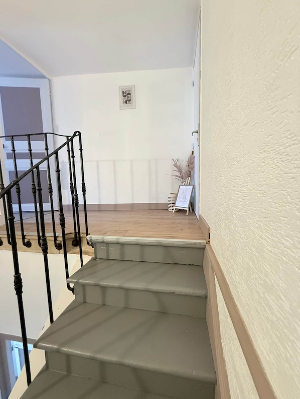 A staircase with a handrail leading to a landing with a framed picture and a vase of dried plants.