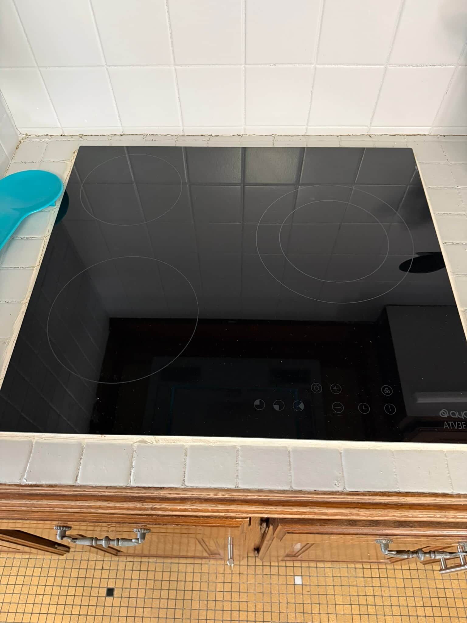 A kitchen with a black stove, white tiled walls, and a wooden countertop.