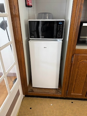 A compact kitchen with a white refrigerator, a microwave on top, and a tiled floor.