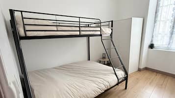 Een stapelbed met een ladder, een klein tafeltje en een hangende lamp in een kamer met houten vloeren en een raam met gordijnen.