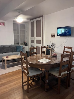 A dining area with a round wooden table, six chairs, and a television mounted on the wall.