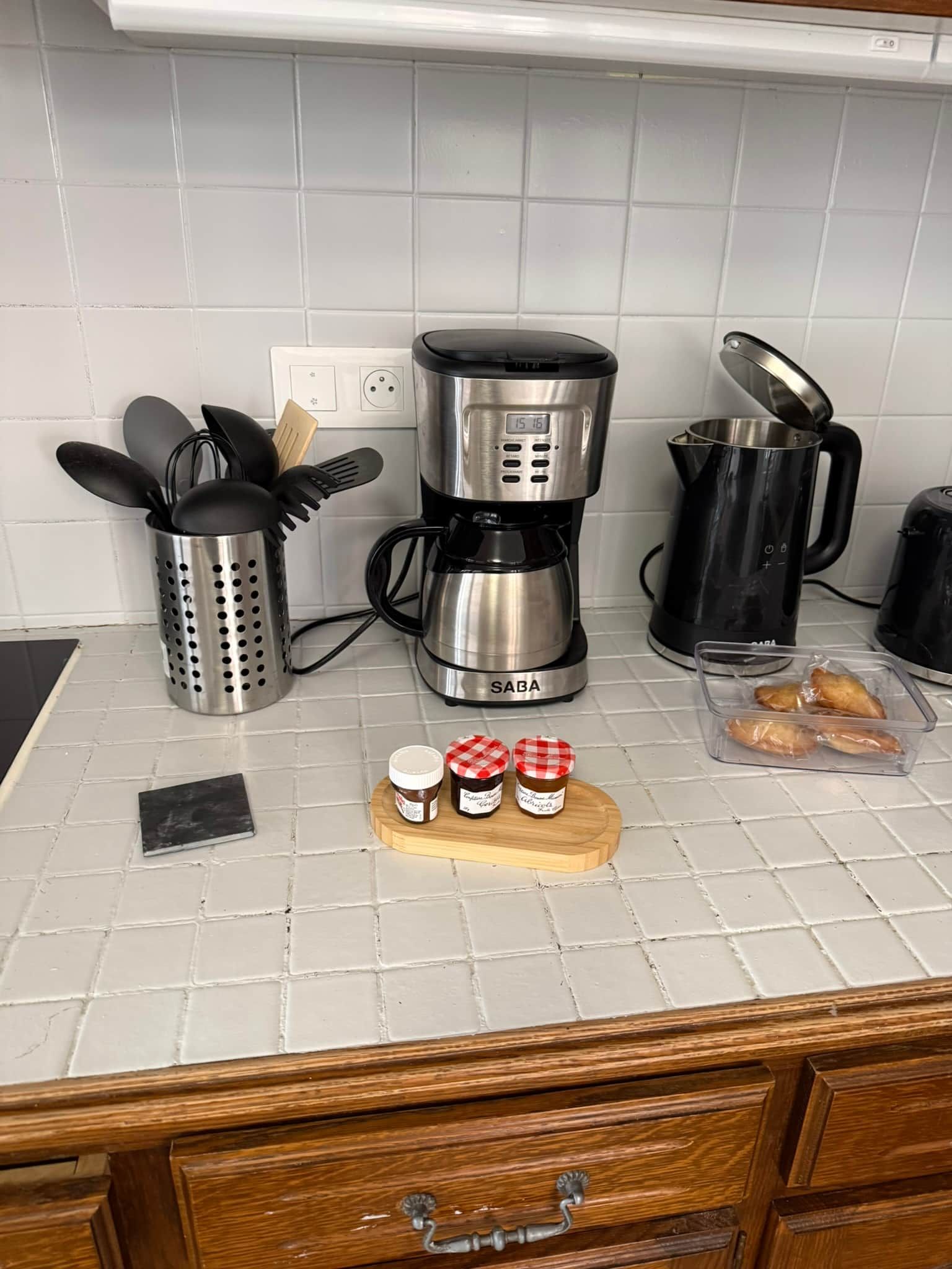 En køkkenbordplade med kaffemaskine, elkedel, sigte, et brød og glas med krydderier.