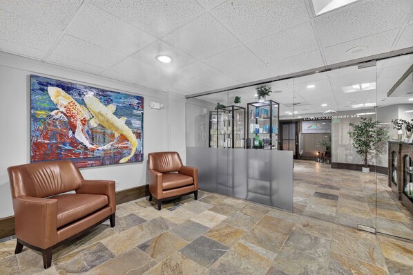 A lobby with a reception desk, two leather chairs, a colorful abstract painting, and a tiled floor. - Charter Ski In Ski Out 2BR (Beaver Creek)