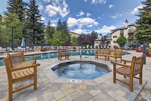A pool area with wooden chairs and a hot tub, surrounded by stone tiles and greenery. - Charter Ski In Ski Out 2BR (Beaver Creek)