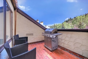 A balcony with a grill, wicker chairs, and a view of a forested hillside. - Charter Ski In Ski Out 2BR (Beaver Creek)