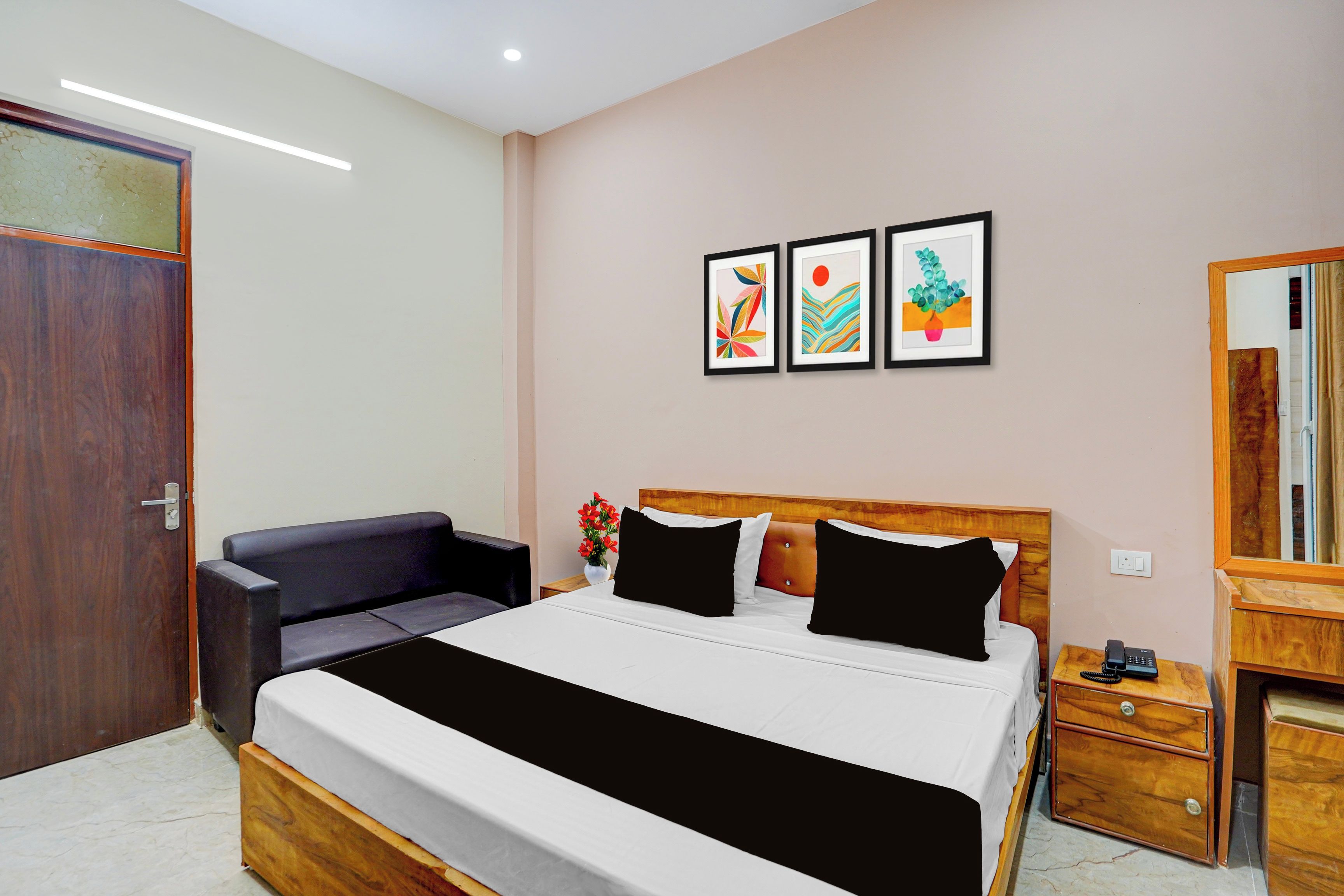 A hotel room with a bed, a bedside table, a chair, a mirror, and artwork on the wall.