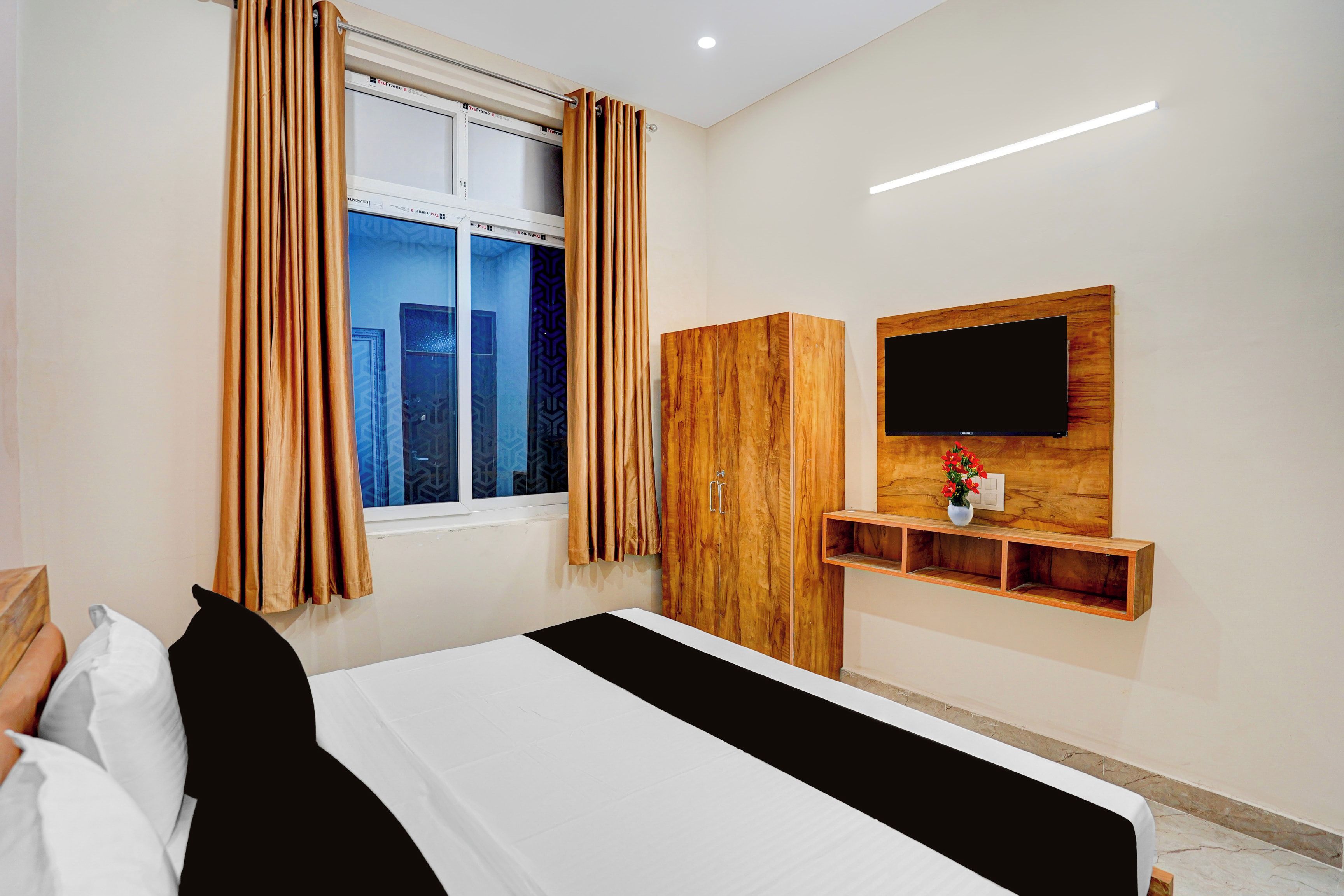 A hotel room with a bed, a wardrobe, a TV mounted on the wall, and a window with curtains.