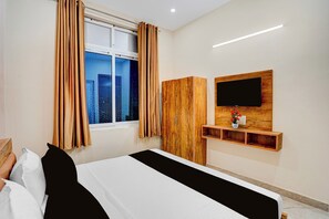 Habitación de hotel con cama, armario, televisor montado en la pared y ventana con cortinas.