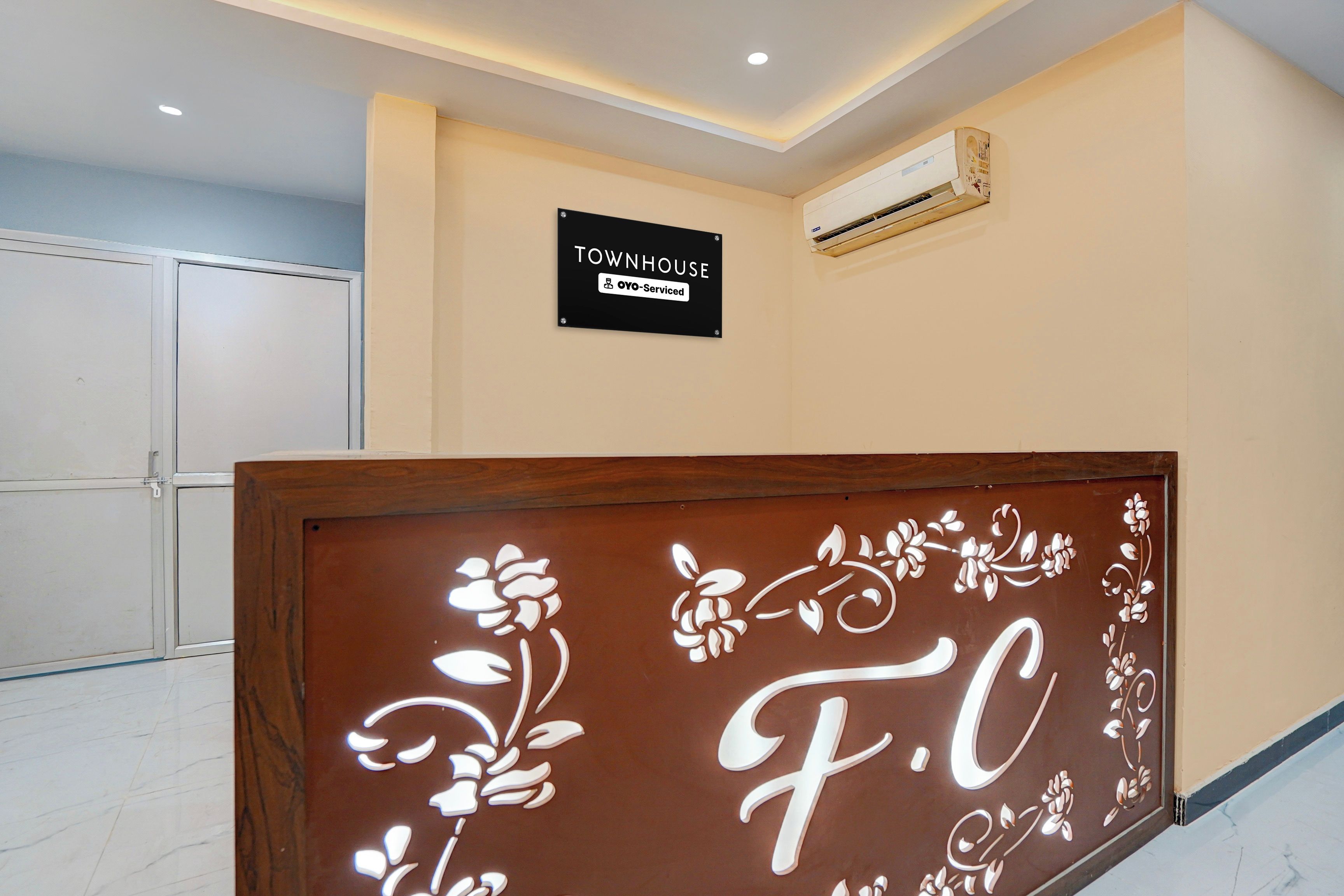 Uma área de recepção com uma placa indicando 'TOWNHOUSE OYO-Serviced' e um painel decorativo com 'F.C'.