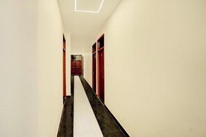 Un pasillo estrecho con piso blanco, puertas rojas e iluminación empotrada en el techo.