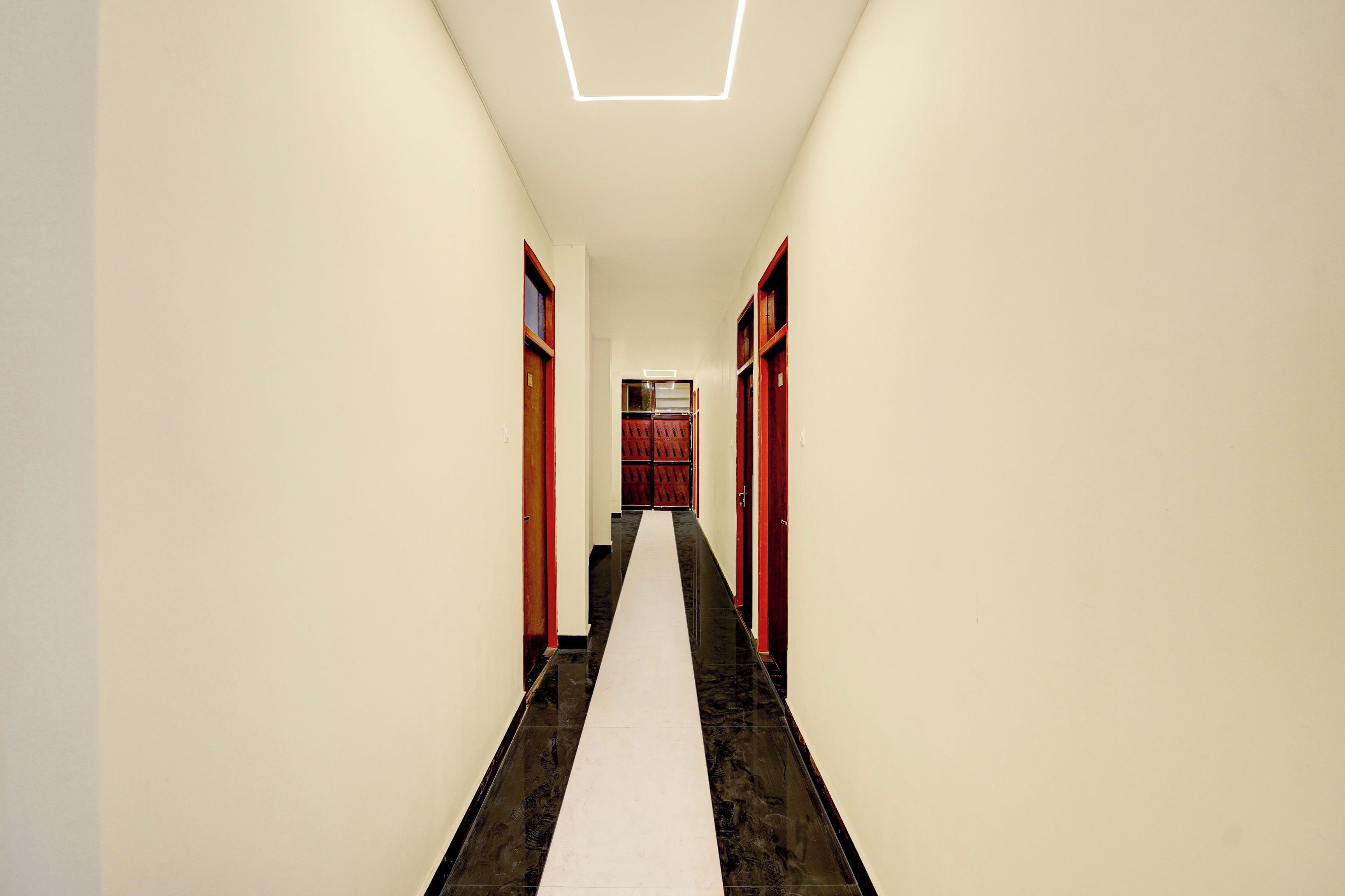 A corridor with a white floor, red doors, and a geometric ceiling light fixture.