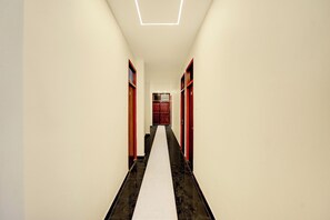 Un pasillo con piso blanco, puertas rojas y un candelabro geométrico en el techo.