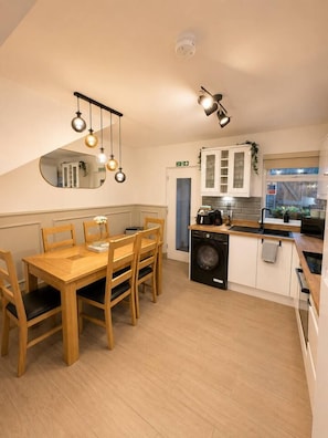 A compact kitchen with a dining area, a washing machine, and a mirror on the wall. - Cosys Corner – Spacious 3-Bedroom Belfast Home (Belfast)