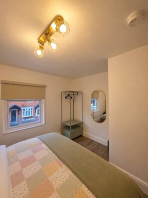 A bedroom with a bed, a window, a mirror, and a hanging light fixture. - Cosys Corner – Spacious 3-Bedroom Belfast Home (Belfast)