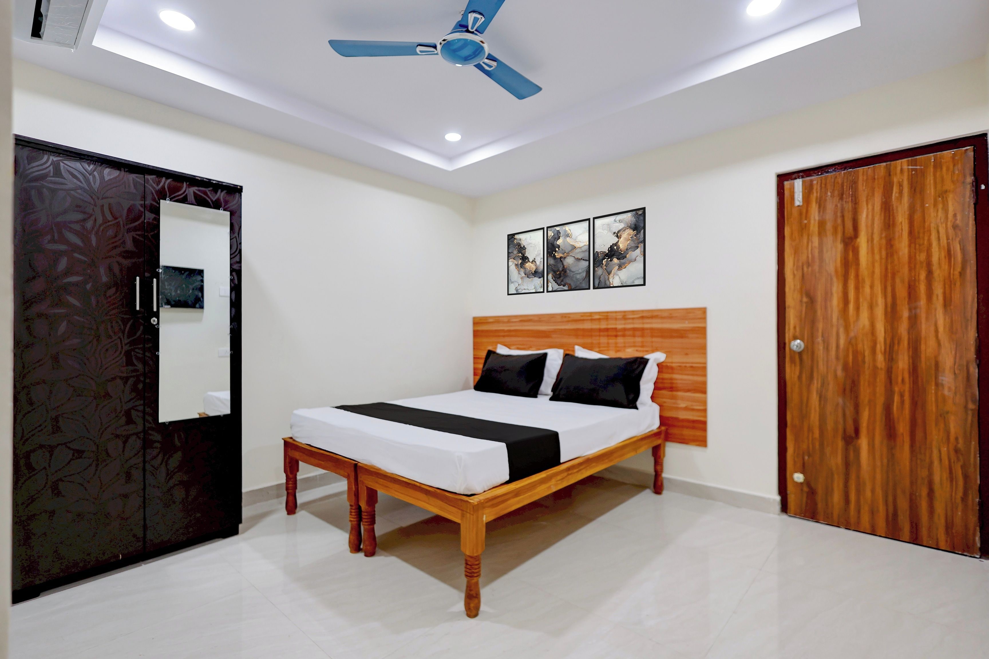 A bedroom with a bed, a ceiling fan, a wooden wardrobe, and a door.