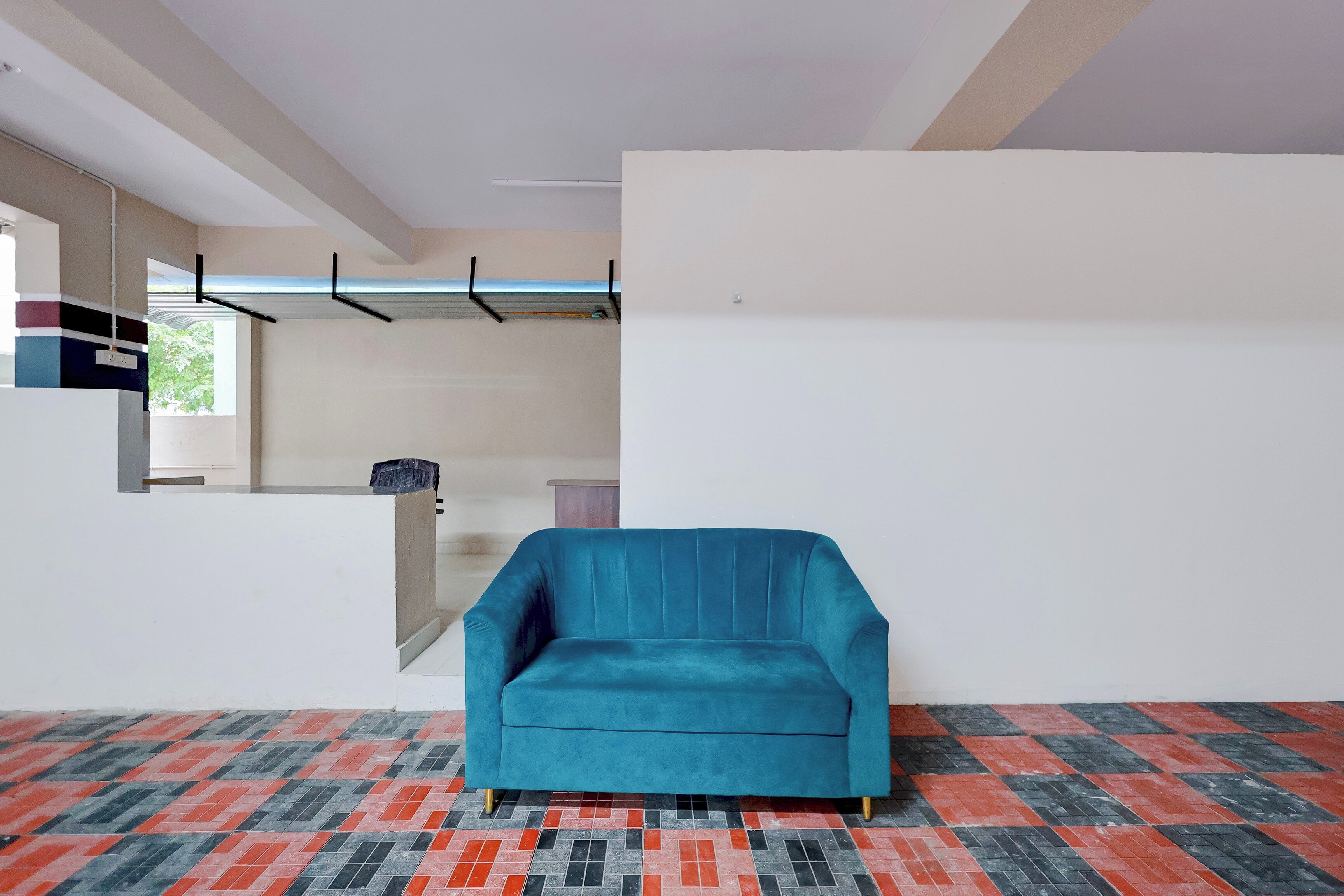 A room with a teal sofa, a patterned floor, a white wall, and a window with a view of greenery.