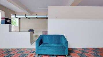 A room with a teal sofa, a patterned floor, a white wall, and a window with a view of greenery.
