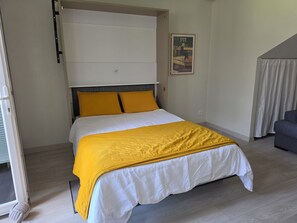 Un dormitorio con cama, cabecera, una obra de arte en la pared y un sofá gris.