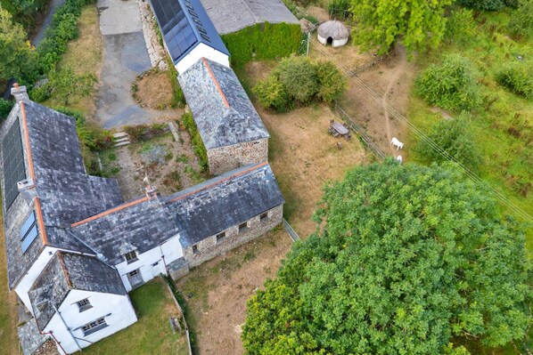 Ein großes Steinhaus mit mehreren Schornsteinen, umgeben von einem Garten mit vielfältigen Pflanzen und einem kleinen weißen Bauwerk.