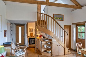 A rustic kitchen with wooden beams, a spiral staircase, and a view of the outdoors. - Moreton Mill Retreat (Launcells)