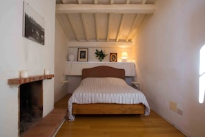 A bedroom with a wooden bed, a fireplace, a shelf with decorative items, and a window. - Top floor flat with terrace overlooking the duomo (Firenze)