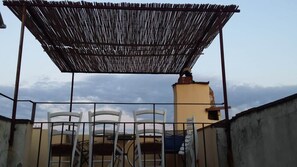 A covered outdoor seating area with metal chairs and a thatched roof. - Top floor flat with terrace overlooking the duomo (Firenze)