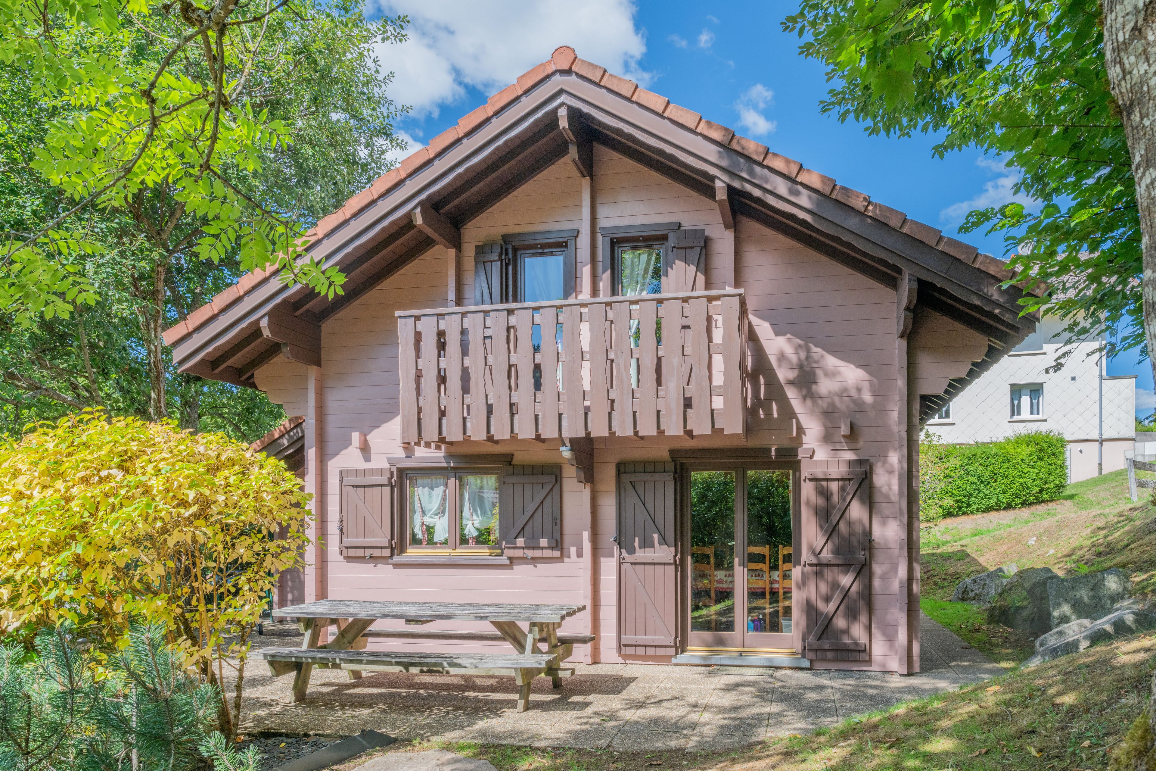 Un chalet en bois doté d’un balcon, d’un banc en bois et d’une porte avec une fenêtre.