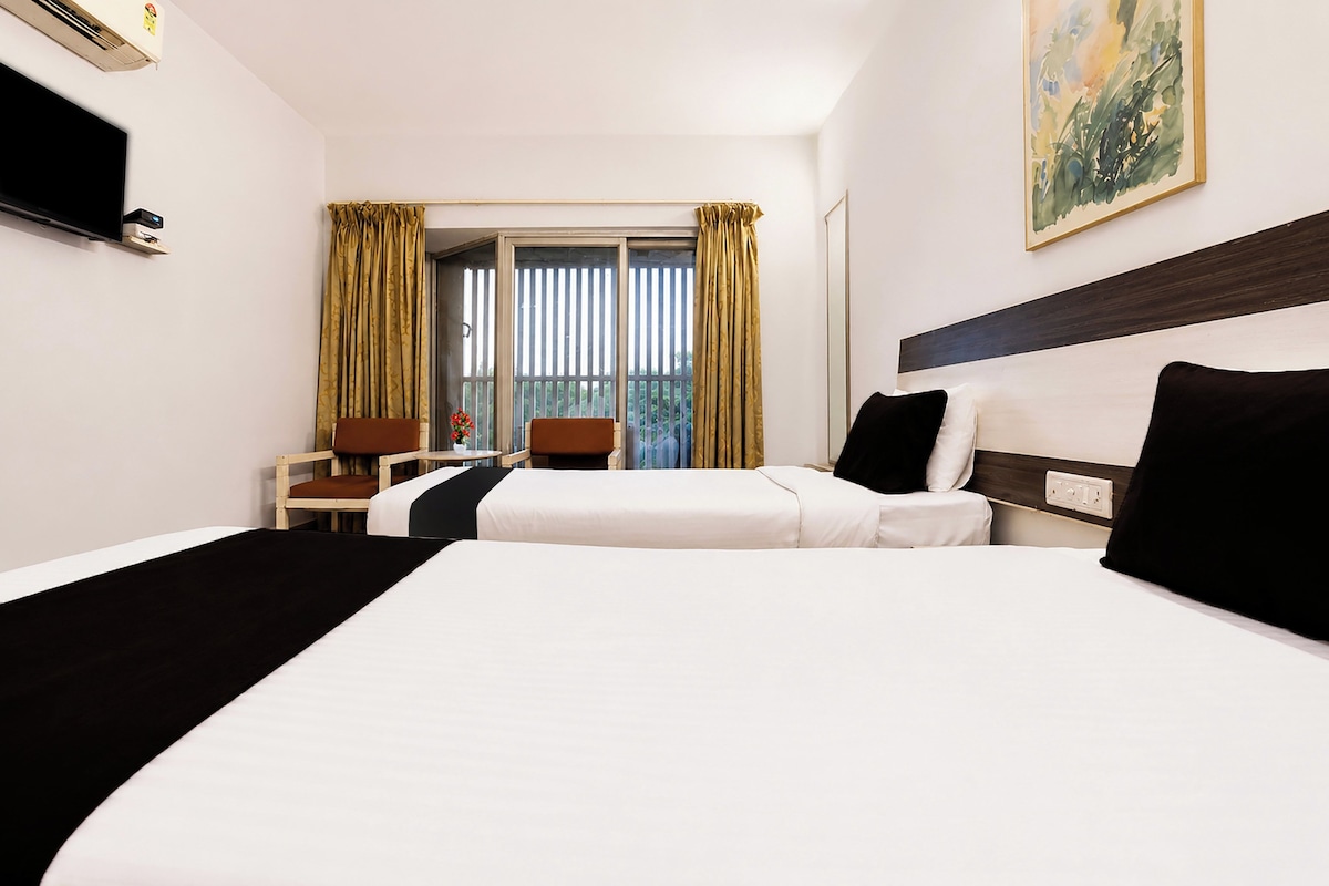 Una habitación de hotel con una cama grande, un escritorio, una silla y un ventanal con cortinas.