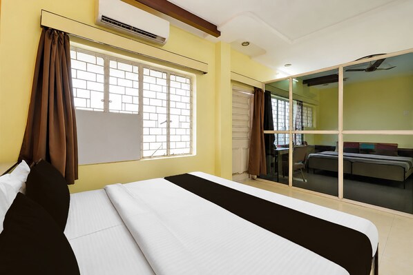 Habitación de hotel con cama, ventana con cortinas, unidad de aire acondicionado y puerta de cristal corredera que da a un balcón.