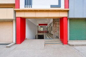 A building entrance with a red and beige facade, a staircase leading to an upper level, and a view into the interior. - Super Hotel O Durg Bus Stand (Ujjain)