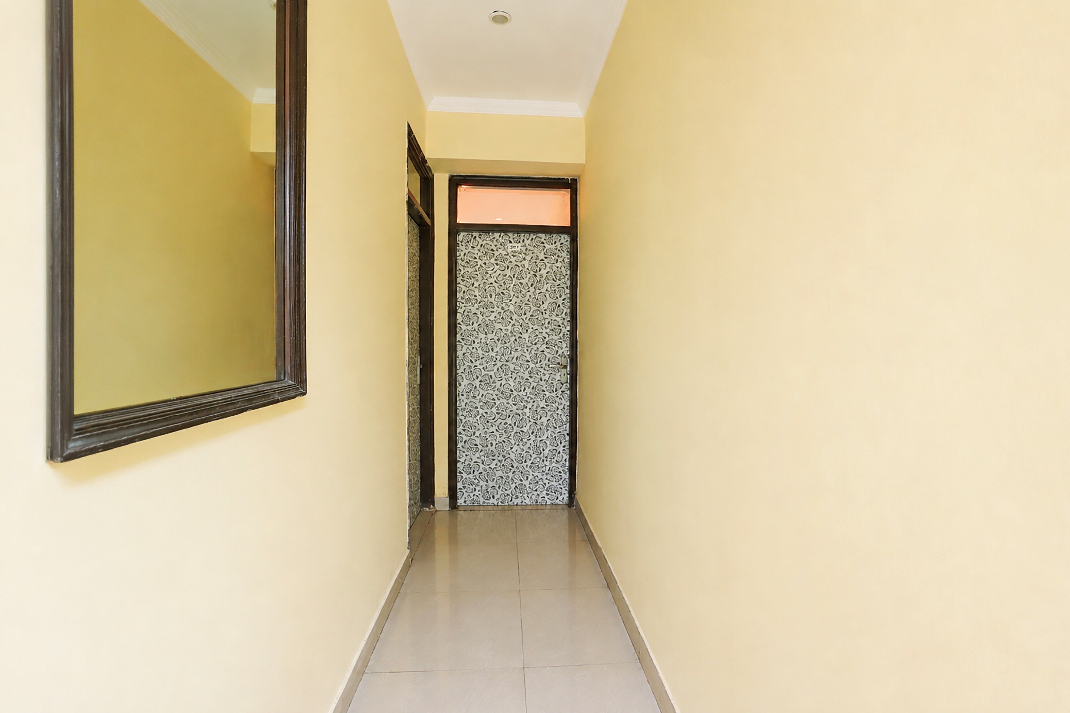 A narrow hallway with a mirror on the left and a patterned door at the end.