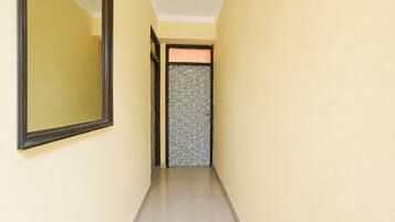 A narrow hallway with a mirror on the left and a patterned door at the end.