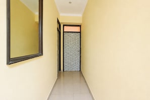 A narrow hallway with a mirror on the left and a patterned door at the end.