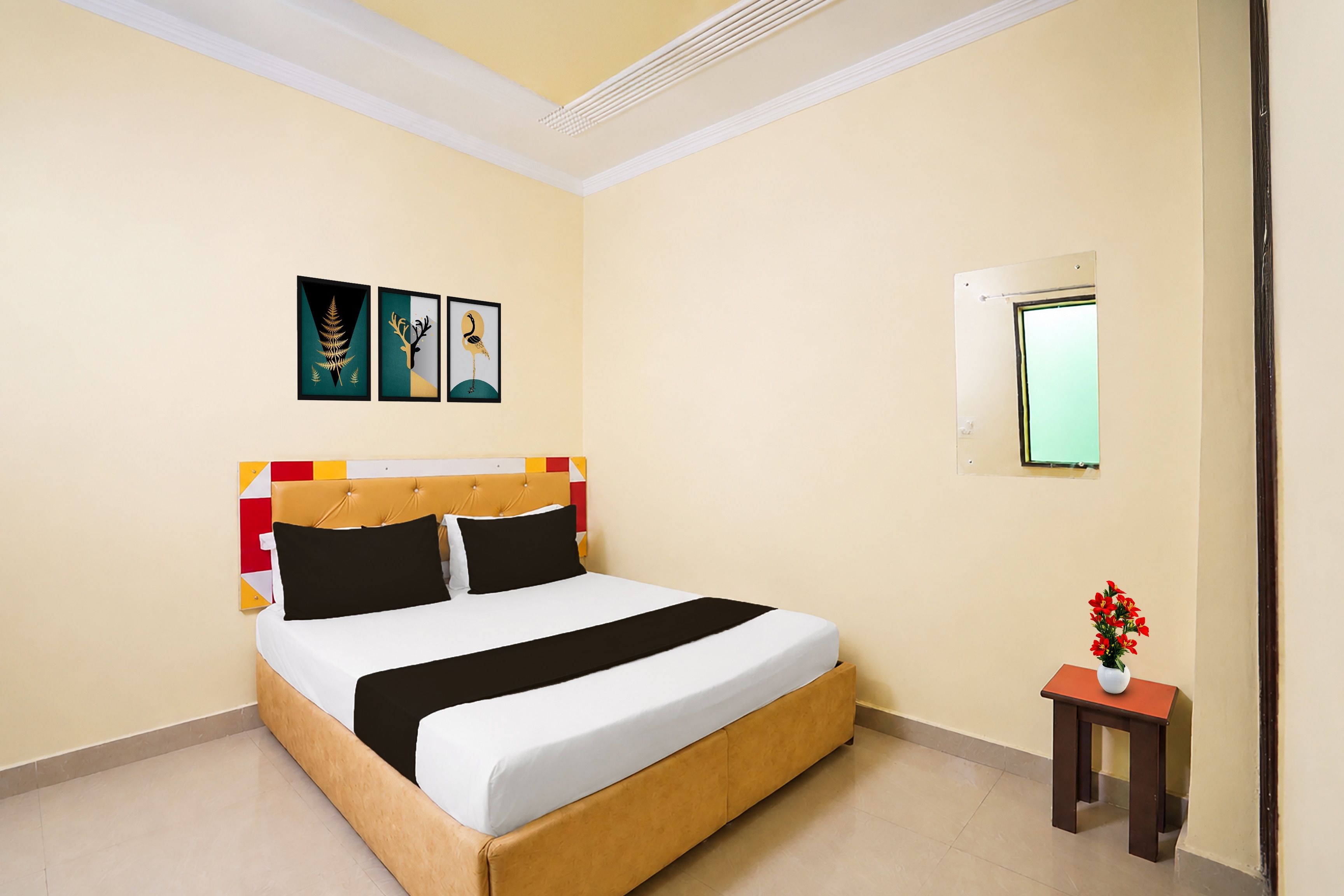 Una habitación de hotel con una cama, una mesita con un florero y obras de arte en la pared.