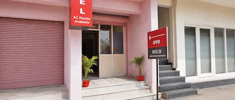A hotel entrance with a red sign indicating AC rooms available and a directional sign for the hotel.