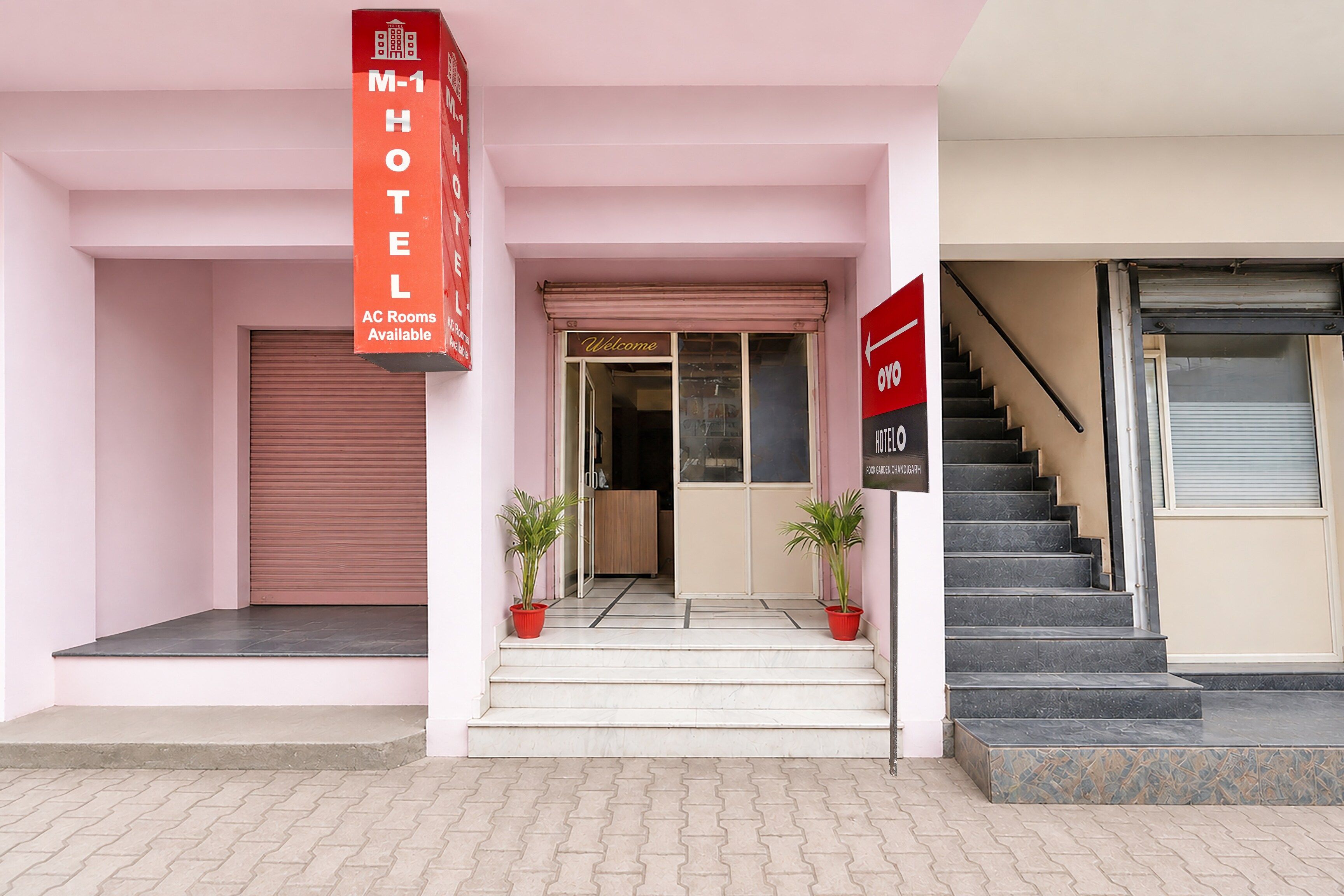 A hotel entrance with a closed shutter, a sign indicating AC rooms available, and a staircase leading to the interior.