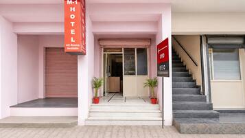 A hotel entrance with a closed shutter, a sign indicating AC rooms available, and a staircase leading to the interior.