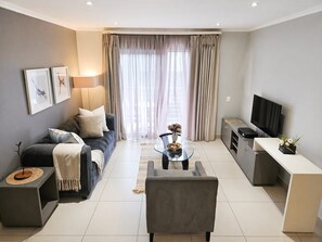 Ein modernes Wohnzimmer mit einer Couch, Couchtisch, Fernseher und einem Essbereich.
