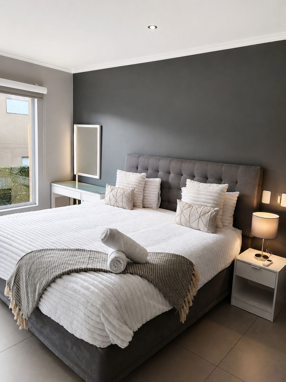 Quarto moderno com uma cama grande, uma mesinha de cabeceira e uma janela.