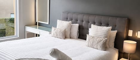 A modern bedroom with a large bed, a bedside table, a nightstand, and a window.