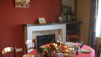 Une salle à manger avec une table rouge mise pour le petit-déjeuner, une cheminée et une bibliothèque.