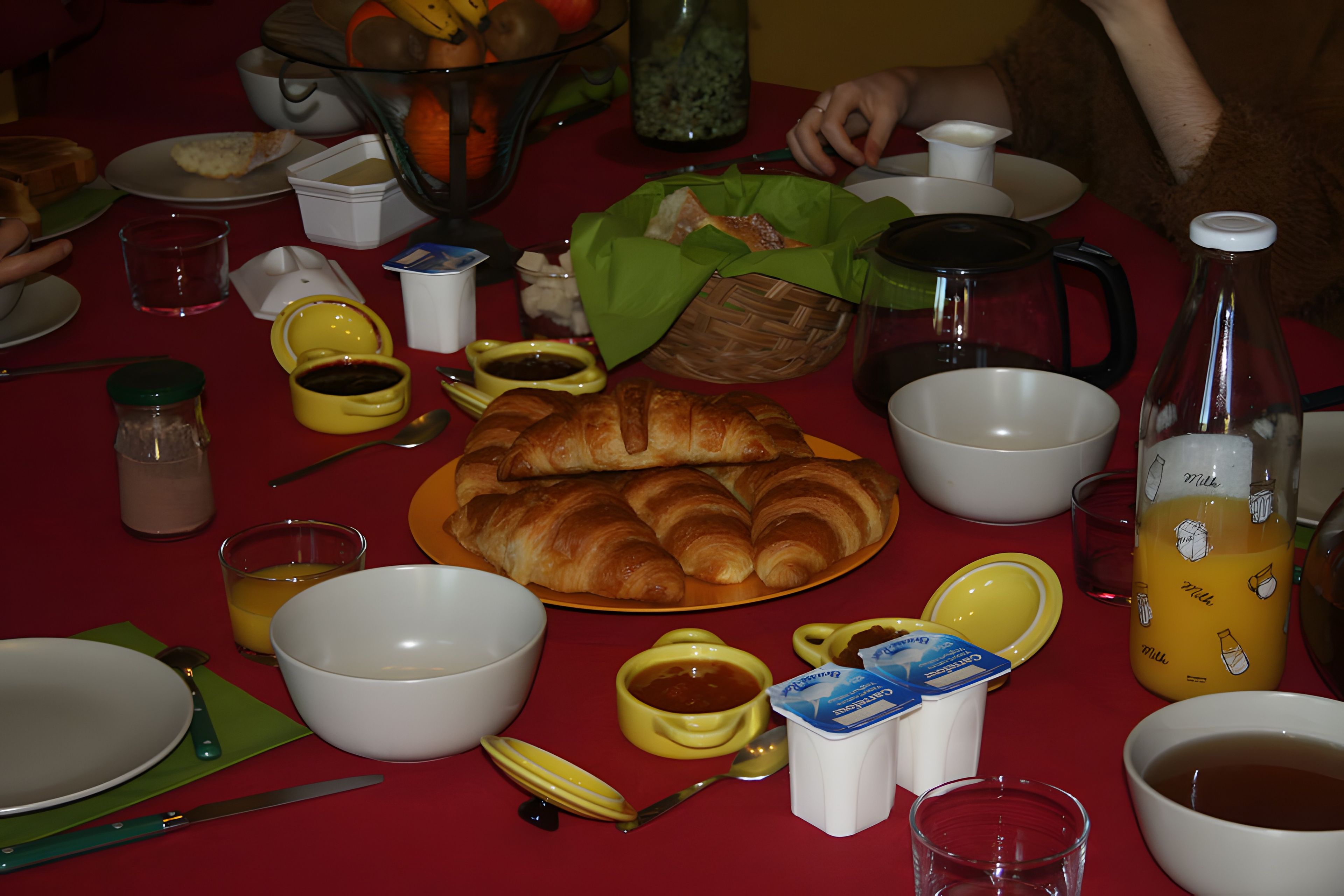 Aamiaispöytä, jossa on erilaisia ruoka-aineita, kuten croissantteja, leipäkori ja maitopullo.